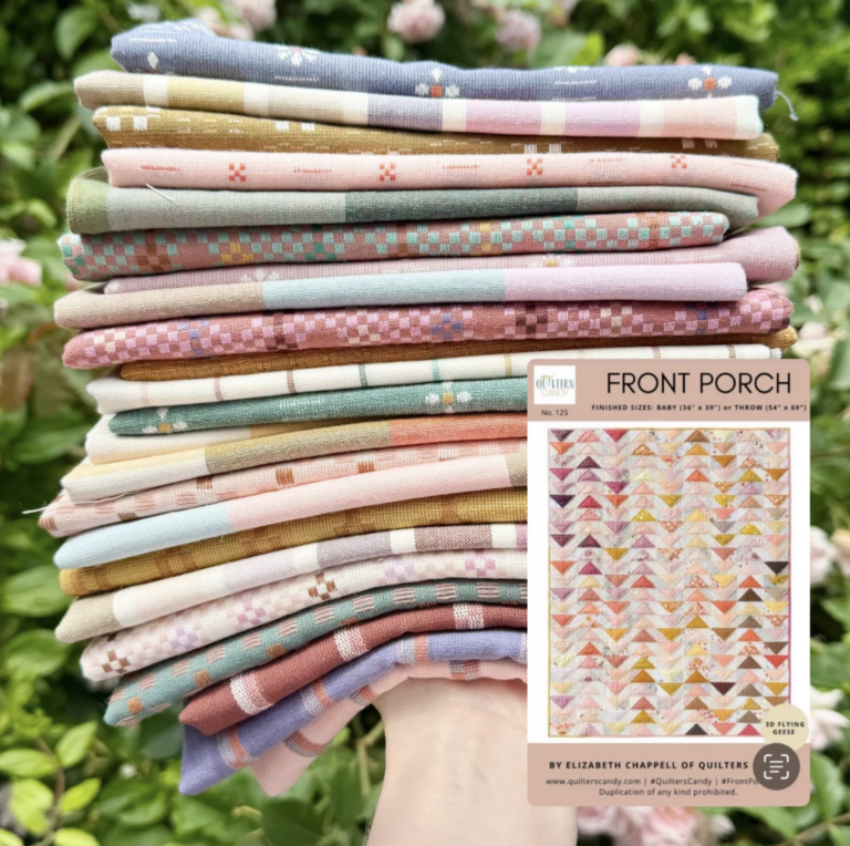 A hand holding a colorful stack of woven fabrics in soft pastels and earthy tones, perfect for the Front Porch quilt pattern. In the foreground, a printed copy of the Front Porch pattern by Elizabeth Chappell of Quilters Candy showcases a flying geese quilt in a soft gradient layout. Lush greenery in the background highlights the vibrant fabric colors.